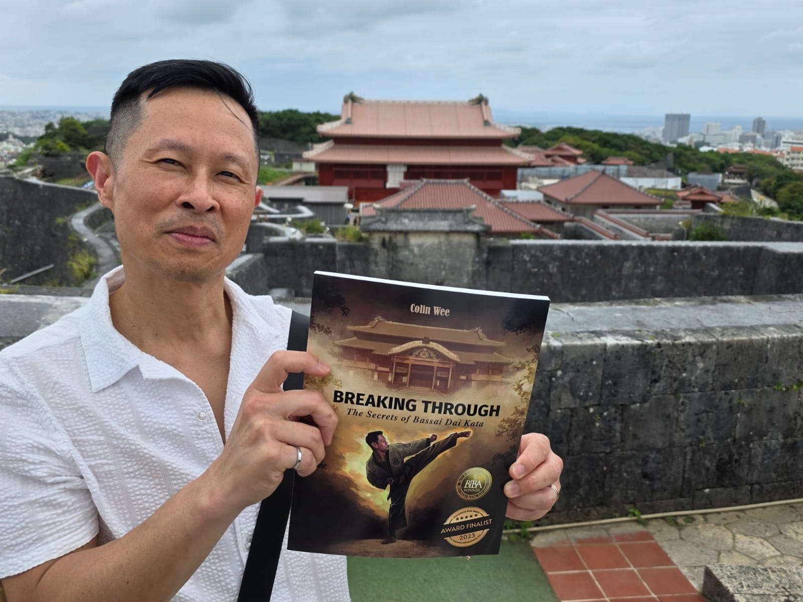 Author Holding Up Book in Front of Shuri Castle, Oct 2026